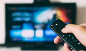 Dłoń trzymająca pilot do telewizora na tle wyłączonego ekranu.