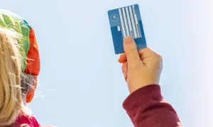 Karta EKUZ dla dziecka – jak wyrobić? Ręka trzyma niebieską kartę EKUZ na tle błękitnego nieba.