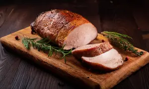 Saftiges Schweinefilet, angebraten und dann im Ofen perfekt gegart, liegt auf einem Holzbrett, garniert mit Rosmarin und Pfefferkörnern.