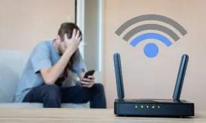 Un homme frustré regarde son téléphone, tandis qu'un routeur wifi est en premier plan. C'est quoi le wifi ? Une connexion sans fil essentielle.