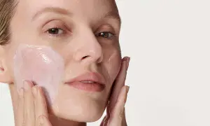 Donna applica una crema idratante sul viso. La sua pelle appare luminosa e sana, pronta per il giorno. Prima scrub o detergente? La scelta è tua per una pelle perfetta.