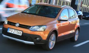 Pomarańczowy Volkswagen Polo Cross w ruchu miejskim, z widocznym kierowcą i innymi samochodami w tle.