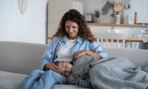 Madre reconforta a su hija, que duerme en su regazo. La menstruación a los 10 años es normal y la madre le ofrece apoyo.