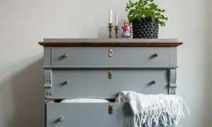 Grå byrå med mässingsdetaljer, en grön växt och en leksaksrobot. Perfekt inspiration för att måla byrå.