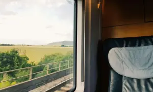 Blick aus dem Zugfenster auf grüne Felder während der zugreise nach wien. Ein bequemer Sitz im Vordergrund.