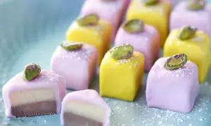 Små, färgglada marsipanbitar med pistage, perfekta för påskgodis recept. En av dem är uppskuren och visar lager av choklad och mandelmassa.