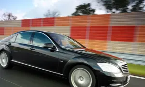Czarny Mercedes S400d pędzi autostradą obok kolorowego ekranu dźwiękochłonnego.