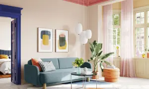 Ein Wohnzimmer mit blauem Sofa, orangefarbenem Hocker und Kunstwerken. Die Decke ist in einem kräftigen Pink gestrichen, was einen schönen Kontrast zur hellen Wandfarbe bildet.