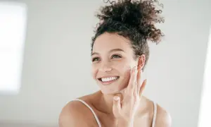 Mujer sonriente aplicándose crema, un paso esencial para el cuidado de piel grasa.
