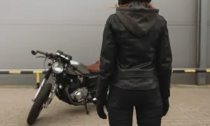 Kobieta w skórzanej kurtce motocyklowej i kasku stoi obok motocykla.