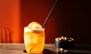 Ein erfrischender Amaretto Sour mit Zitrone und Eiswürfeln, daneben eine Schale Erdnüsse.