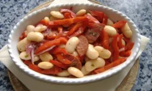 Ein herzhafter spanischer Bohnensalat mit weißen Bohnen, roten Paprikastreifen und Chorizo in einer weißen Schüssel.