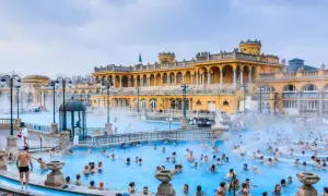 Ludzie kąpią się w gorących źródłach, które są jednymi z najlepszych term w Europie, z piękną, żółtą architekturą w tle.