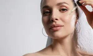Mujer con toalla en la cabeza aplica gotas de sérum con péptidos para la cara, buscando una piel radiante y rejuvenecida.
