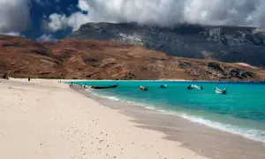 Plaża na Sokotrze, turkusowa woda, góry w tle. Kilka łodzi czeka na podróżnych, marzących o lotach na tę rajską wyspę.