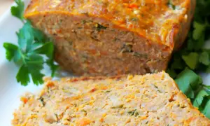 Pyszna pieczeń z mięsa mielonego, pokrojona w plastry, z widocznymi kawałkami marchewki i ziół, udekorowana natką pietruszki.