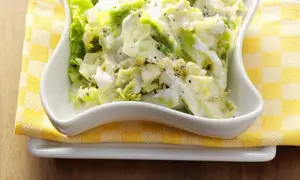 Cremiger Weißkohlsalat, ein einfaches wirsing rezept, serviert in einer weißen Schüssel auf gelb-weiß karierter Serviette.