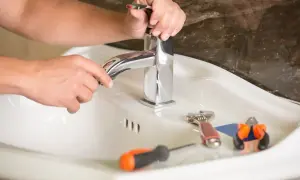 Ręce majsterkowicza naprawiają kapiący kran. Obok leżą klucz, śrubokręt i kombinerki.
