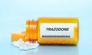 Pomarańczowa butelka z tabletkami trazodone, kilka białych tabletek wysypanych na niebieskie tło.