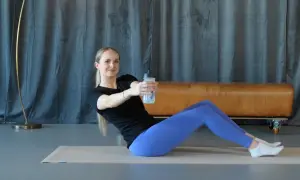 Frau macht isometrisches Training auf einer Matte, hält eine Wasserflasche und dreht den Oberkörper.