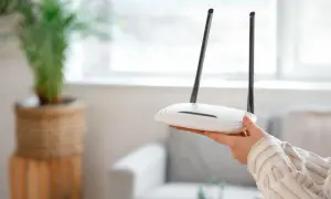 Dłoń trzyma biały router z dwiema antenkami. Może to być pierwszy krok, jak zresetować router, gdy internet przestaje działać.
