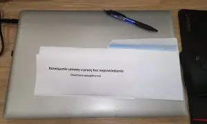 Na laptopie leżą dokumenty z napisem "Rozwiązanie umowy o pracę bez wypowiedzenia (Zwolnienie dyscyplinarne)". Obok długopis i myszka.