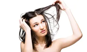 Jeune femme aux cheveux gras, se touchant la tête, l'air interrogateur. Pourquoi ces cheveux gras ?
