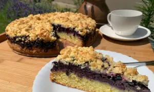 Ein saftiger Heidelbeerkuchen mit Streuseln, ein Stück auf einem Teller, daneben eine Tasse Tee.