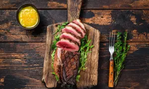 Perfekt gegarte Entenbrust mit rosa Kern, auf einem Holzbrett mit Rucola, dazu eine Schale mit Sauce und ein Gabel. Die Kerntemperatur der Entenbrust ist ideal.