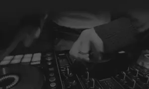Dłoń DJ-a manipulująca pokrętłami na konsoli do miksowania muzyki.