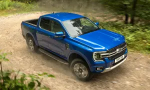 Blå Ford Ranger laddhybrid kör på en grusväg genom en skog.