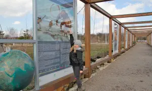 Dziewczynka wskazuje na tablicę informacyjną o prehistorii, jedną z atrakcji Jaworzna. Obok globus.