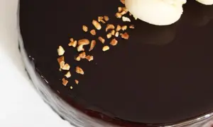 Gâteau au glacage chocolat brillant, parsemé de noisettes concassées et décoré de macarons.