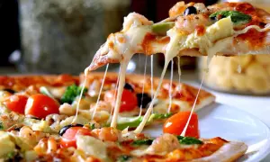 Rozciągający się ser z kawałka pizzy, na której widać krewetki, pomidorki i oliwki. Ciasto na pizzę wygląda apetycznie.