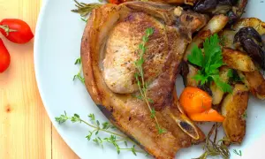 Une côte de porc juteuse, accompagnée de pommes de terre rôties, d'aubergines et de carottes, garnie d'herbes fraîches.