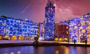Edifici illuminati da proiezioni natalizie sul lago di Garda a dicembre, con cielo stellato e una scia luminosa.