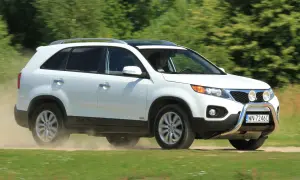 Białe Kia Sorento 1 zderza się z kurzem na drodze gruntowej, jadąc przez zielone pola.