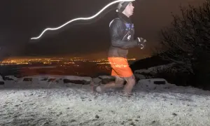 Un coureur nocturne s'entraîne pour la Saintélyon sur un sentier enneigé, la ville illuminée en arrière-plan.