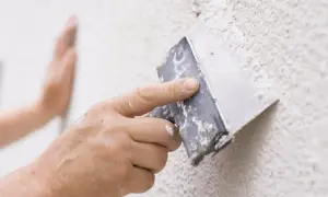Handen använder en spackel för att laga puts på en vägg.