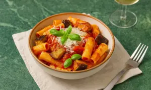 Eine Schüssel Pasta alla Norma mit Auberginen, Tomatensauce und Basilikum, garniert mit geriebenem Käse.