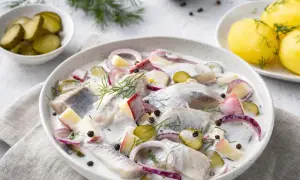 Marinierter Hering mit Äpfeln, Zwiebeln und Dill in cremiger Sauce, garniert mit Pfefferkörnern. Dazu Pellkartoffeln und Gewürzgurken.