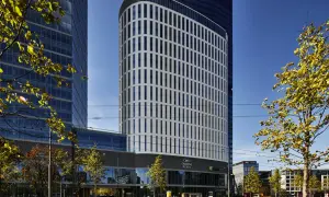 Nowoczesny budynek Crowne Plaza, część kompleksu Holiday Inn Warszawa, z charakterystyczną, falistą fasadą i zielenią wokół.