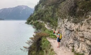 Wanderer genießen die Achensee Umrundung auf einem schmalen Pfad entlang steiler Felswände mit Blick auf den See und die Berge.