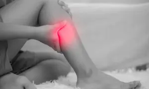 Una persona si tiene la gamba, evidenziata in rosso, per un dolore acuto. Le fitte gambe sono un segnale da non ignorare.