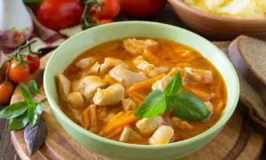 Aksamitny gulasz z piersią z kurczaka z marchewką, udekorowany bazylią. Obok kromki chleba i miska purée ziemniaczanego.