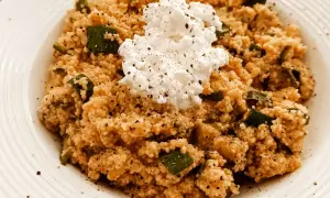 Un piatto di cous cous con zucchine e una generosa porzione di fiocchi di latte al centro, condito con pepe nero.