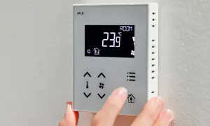 Dłoń naciska przyciski na termostacie, pokazując temperaturę 23.9°C. Dowiedz się, jak włączyć pompę ciepła, korzystając z intuicyjnego panelu sterowania.