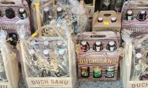 Drewniane skrzynki i opakowania z butelkami regionalnego piwa "Duch Sanu", ozdobione sznurkiem i folią.