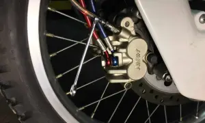 Zbliżenie na zacisk hamulcowy motocykla z przewodami hamulcowymi i kluczem.