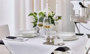 Vacker dukning med vita tallrikar, vinglas och ljus. Frågan "hur stor duk ska man ha" besvaras här med en duk som täcker bordet elegant.